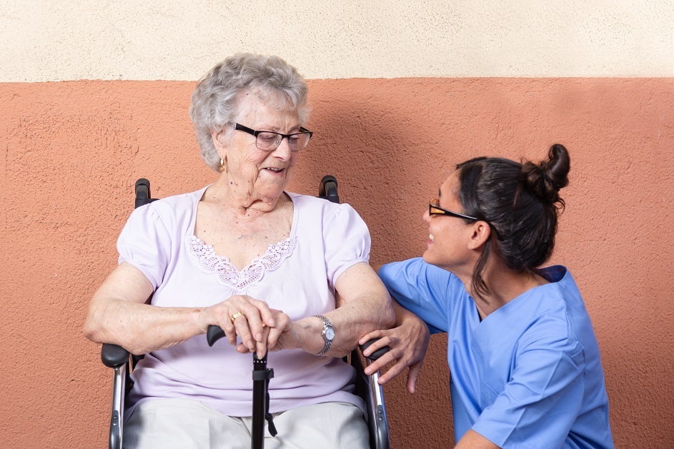 Caregiver kneeling next to elderly woman in a wheelchair
