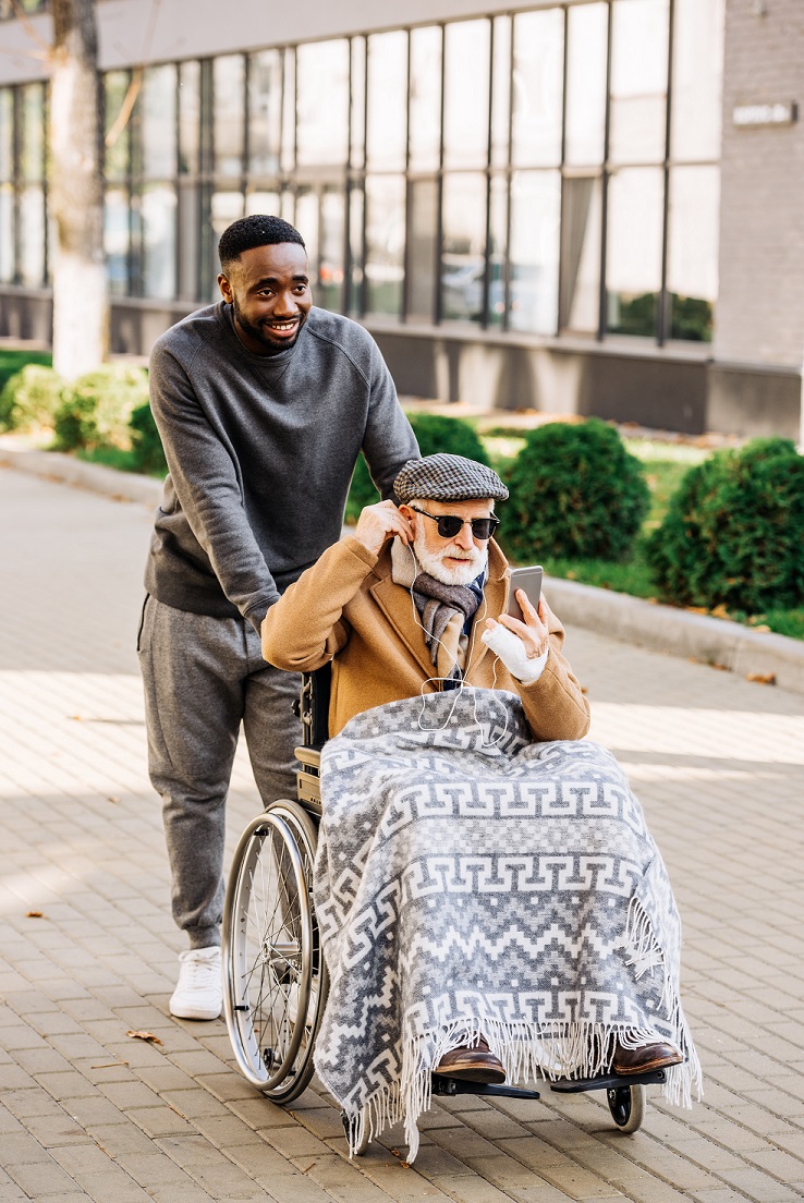 Male caregiver pushes elderly man in a wheelchair