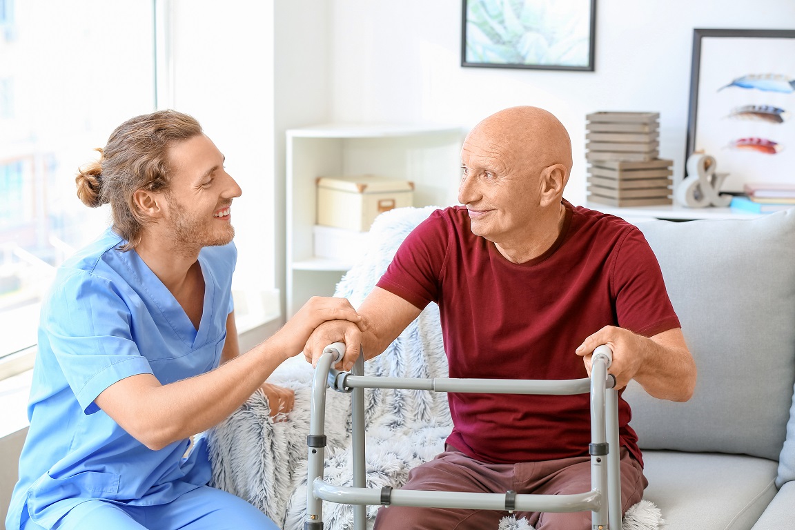 Male caregiver sits next to an elderly man with a walker
