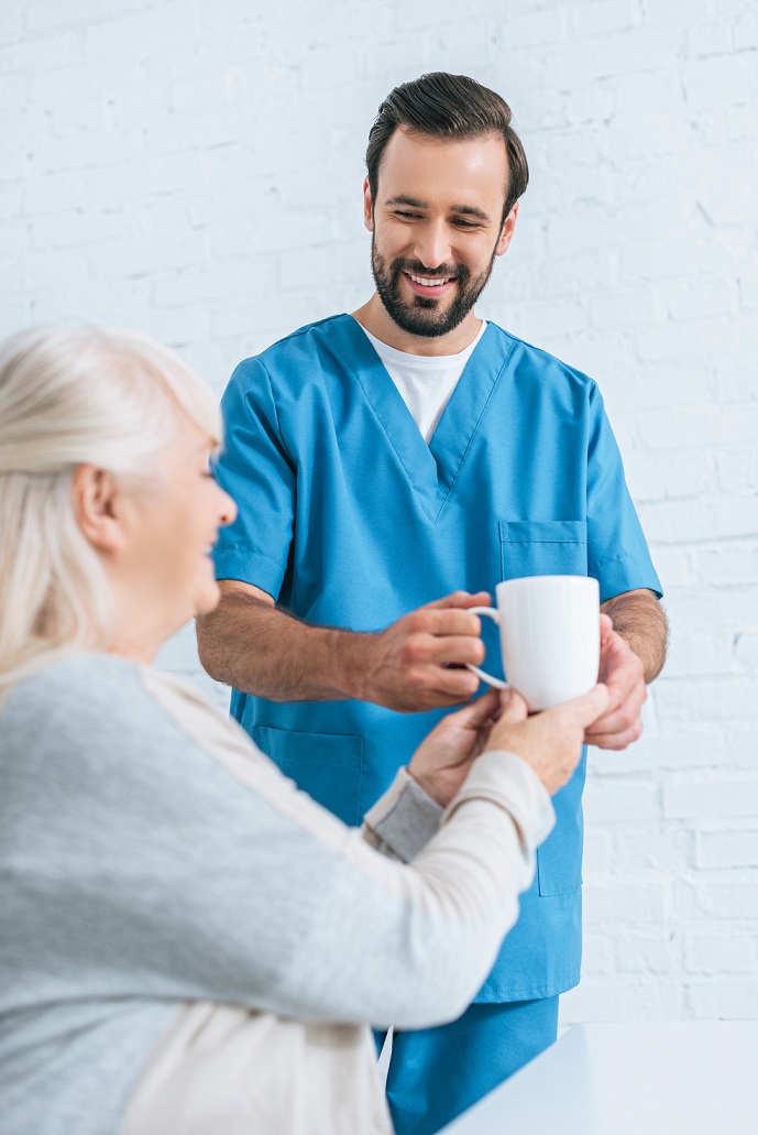 Male caregiver gives elderly woman a cup of coffee